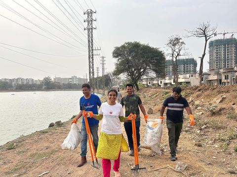 Four volunteers with rakes and sacks walking along the lake